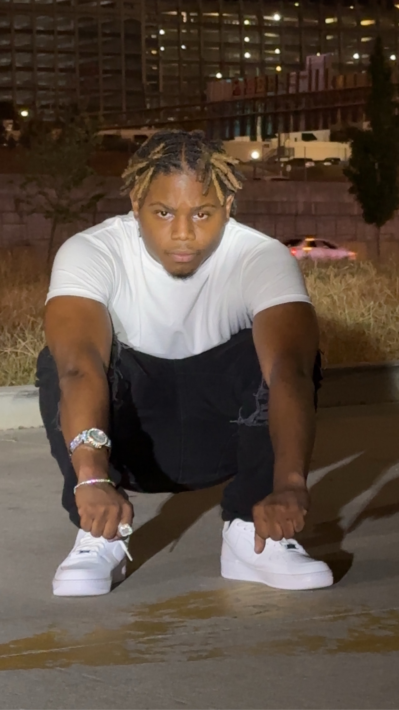 BABYSCAR crouched down at night in a white tee and white sneakers, staring into the camera