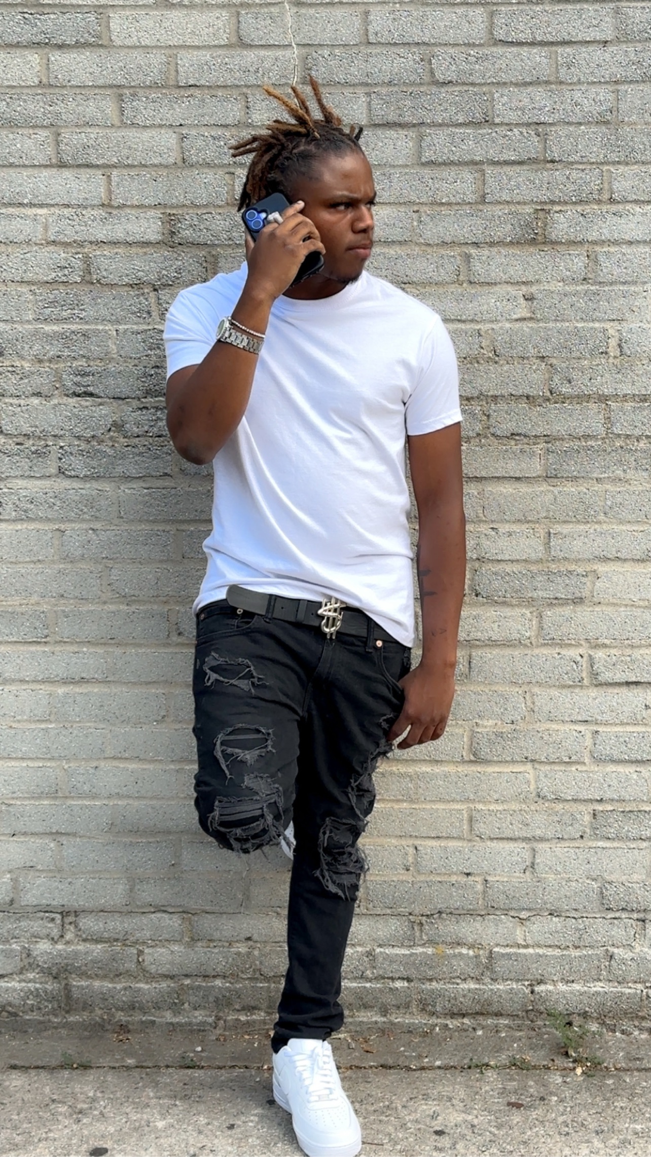 BABYSCAR in a white tee and ripped black jeans, on the phone against a brick wall